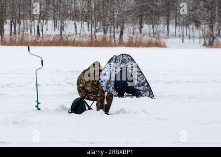 Pesca invernale. Pescatori sul ghiaccio del bacino idrico con una tenda e accessori per la pesca Foto Stock