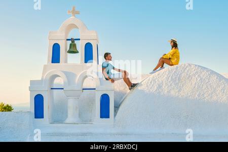 Giovani coppie di turisti uomini e donne visitano Oia Santorini Grecia in una giornata di sole durante l'estate con case e chiese imbiancate di bianco, l'isola greca Cicladi del Mar Egeo Foto Stock