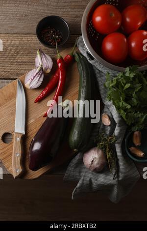 Cucinare ratatouille. Verdure, grani di pepe, erbe aromatiche e coltello su tavola di legno, stesa piatta Foto Stock