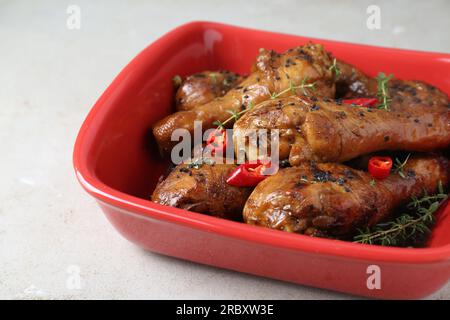 Cosce di pollo glassate in salsa di soia con sesamo nero, peperoncino e timo su un tavolo leggero, primo piano Foto Stock