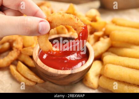 Donna che immerge l'anello di cipolla nel recipiente con il saporito ketchup al tavolo, primo piano Foto Stock