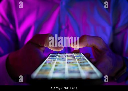 uomo che scorre lo schermo del telefono cellulare in una stanza buia con luci al neon. navigazione in internet, social media e marketing Foto Stock