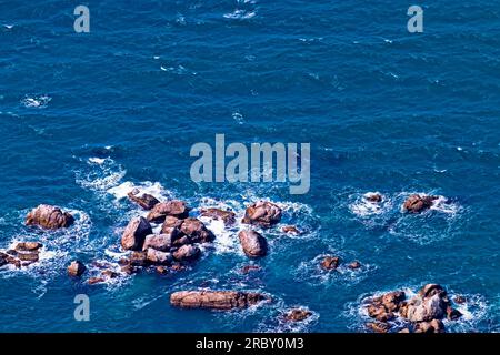 Una barriera corallina sollevata nelle acque costiere e le onde si infrangono sulle rocce e sulla schiuma Foto Stock