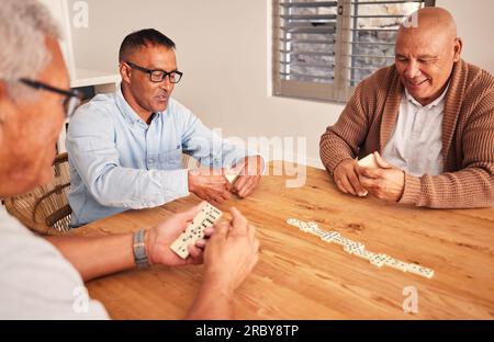 Uomini anziani, amici e tavolo per il gioco domino, la gara e felice insieme con la strategia in pensione. Persone, gruppi anziani e relax con concentrazione Foto Stock