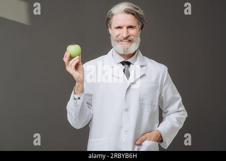 Medico maturo sorridente che tiene una mela e guarda nella macchina fotografica Foto Stock