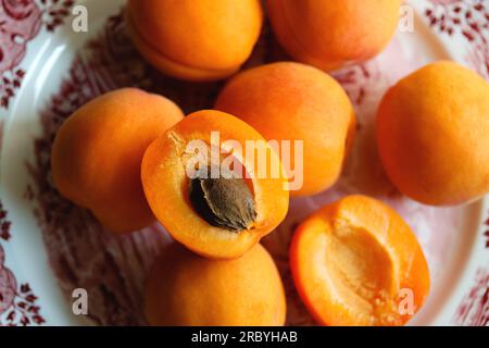 Deliziose albicocche mature in un piatto da vicino sul tavolo. Pila di albicocche d'arancia fresche interi e una metà di albicocca con un seme su un piatto di E. Foto Stock