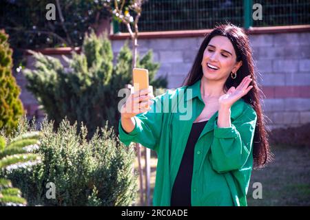 Beautiful Woman dice addio alla fotocamera mentre videochiacchiera all'aperto Foto Stock