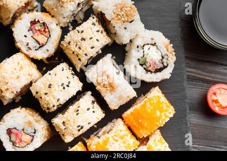 Set di panini sushi con salmone, tonno, caviale, semi di sesamo su un piatto di ardesia nero, vista dall'alto, primo piano. Foto Stock