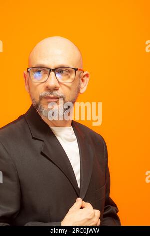 Uomo elegante in giacca, con beared, calvo e occhiali da vista. Isolato su sfondo arancione Foto Stock