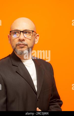 Uomo elegante in giacca, con beared, calvo e occhiali da vista. Isolato su sfondo arancione Foto Stock