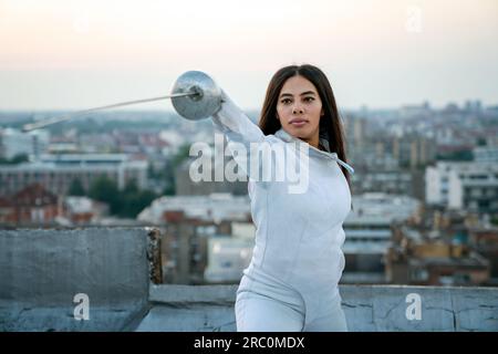 Donna in costume da scherma bianco che pratica all'aperto. Sport, allenatore professionale, stile di vita sano. Foto Stock