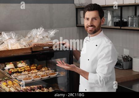 panettiere professionale vicino alla vetrina con pasticceria in negozio Foto Stock