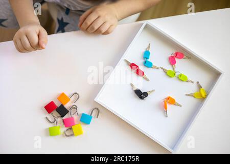 Il bambino lavora con materiale Montessori con serrature colorate. Raccoglie i tasti. Sviluppa le abilità motorie fini. Foto Stock