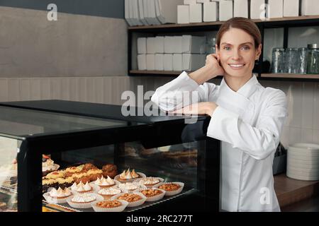 panettiere professionale vicino alla vetrina con pasticceria in negozio Foto Stock