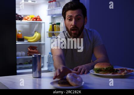 Uomo che prende la ciambella in cucina di notte. Cattiva abitudine Foto Stock