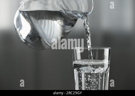 Versare l'acqua dalla caraffa nel vetro su sfondo sfocato, primo piano Foto Stock