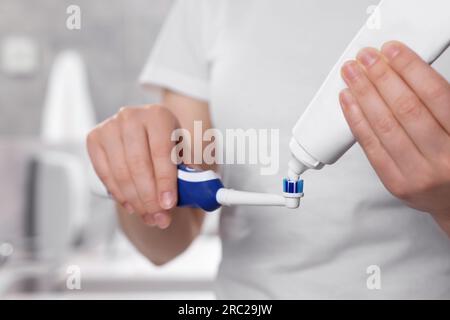 Donna che strizza dentifricio dal tubo allo spazzolino elettrico in bagno, primo piano Foto Stock