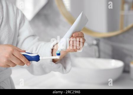 Donna che strizza dentifricio dal tubo allo spazzolino elettrico in bagno, primo piano Foto Stock