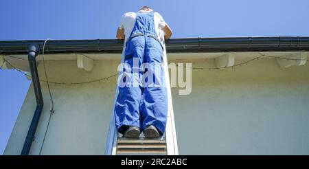 Il tetto della casa ripara il tetto. Il tetto al lavoro. Tetto in piedi sulla scala di metallo. Foto Stock