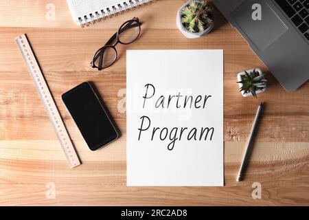 Carta con parole Partner Program su tavolo da ufficio in legno. Ambiente di lavoro con notebook Foto Stock