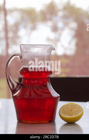 Composta rossa in un decanter di vetro. Bevanda estiva con frutti di bosco e frutta. Accanto al tavolo ci sono gli ingredienti per la bevanda alla frutta. Foto Stock