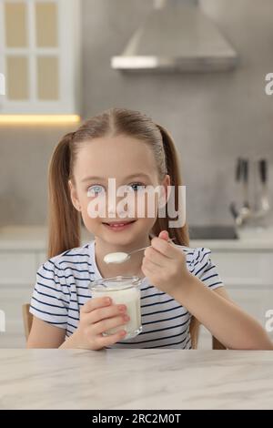 Ragazza carina con yogurt gustoso al tavolo di marmo bianco in cucina Foto Stock