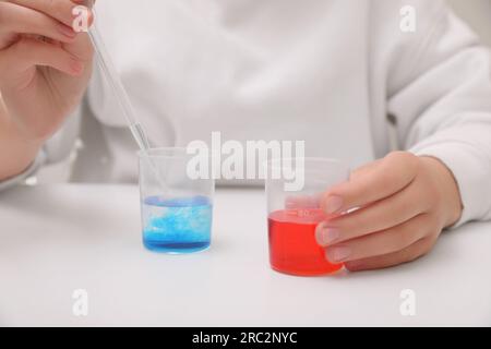 Ragazza che mescola liquidi colorati al tavolo bianco in interni, primo piano. Set di esperimenti chimici per bambini Foto Stock
