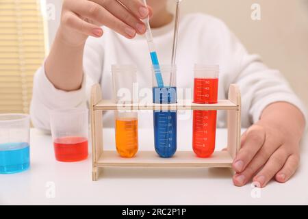 Ragazza che mescola liquidi colorati al tavolo bianco in interni, primo piano. Set di esperimenti chimici per bambini Foto Stock