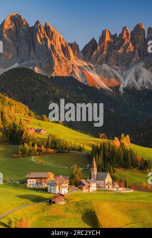 Un'immagine verticale di un tramonto autunnale presso la famosa chiesa e villaggio di Santa Maddalena di fronte alle cime delle Dolomiti di Odle Foto Stock