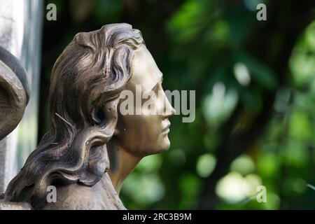 Profilo di un volto di un angelo dorato su una tomba in un cimitero su sfondo verde sfocato Foto Stock