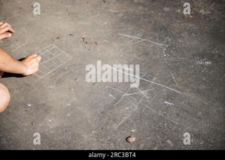 Felice infanzia. Bambini caucasici che giocano all'aperto durante il giorno, graffiando il terreno con una roccia per giocare al classico gioco del TIC-tac-toe. Foto Stock