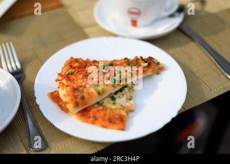 Due fette di pizza con salsiccia e carne su un piatto, sul tavolo. cibo di strada Foto Stock