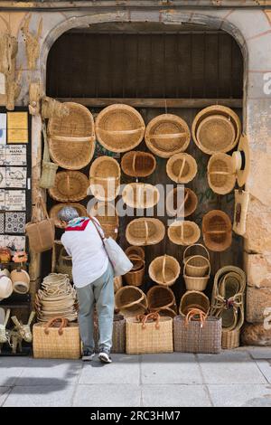 Shopping femminile in vacanza, vista posteriore in estate di una turista matura che guarda cesti in vendita in una strada nella storica città di Segovia, Spagna Foto Stock