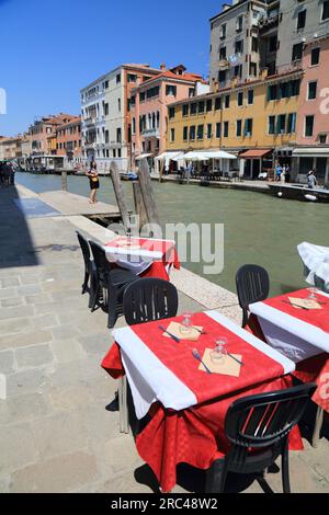 VENEZIA, ITALIA - 22 MAGGIO 2023: Tavoli da caffè accanto al Canale di Cannaregio a Venezia, Italia. Venezia è un sito patrimonio dell'umanità dell'UNESCO. Foto Stock