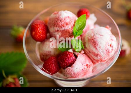 Palle di gelato alla fragola fatto in casa in una ciotola su un tavolo di legno. Foto Stock