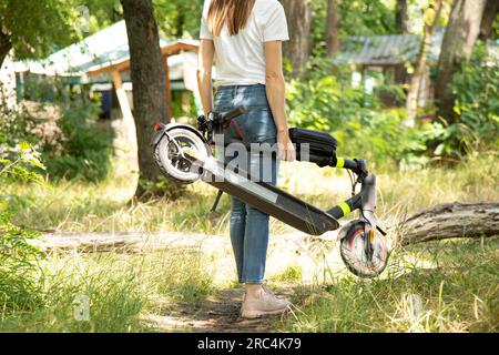 Una ragazza tiene in mano uno scooter elettrico nei parchi in Ucraina in estate, trasporto elettrico urbano Foto Stock