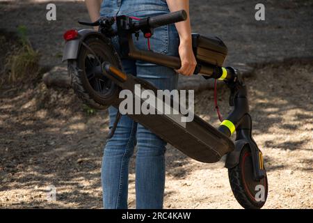 Una ragazza tiene in mano uno scooter elettrico nei parchi in Ucraina in estate, trasporto elettrico urbano Foto Stock