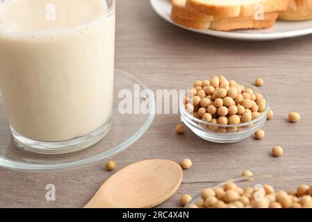 Dettaglio della ciotola con semi di soia secchi su tavola di legno con prodotti di soia alternativi intorno, come bevande e pane. Vista elevata. Foto Stock