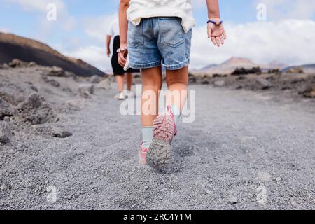 Bambino anonimo in scarpe da ginnastica seguendo un uomo irriconoscibile su un terreno arido e asciutto mentre cammina vicino l'uno all'altro nella soleggiata giornata estiva contro il cielo blu Foto Stock
