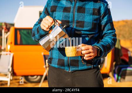 Coltiva un uomo irriconoscibile in abiti casual in piedi e versa una bevanda calda nel deserto collinare nel canyon Rojo Teruel Spagna Foto Stock