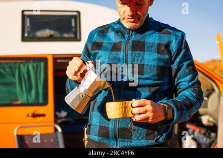 Uomo maturo pensivo in abiti casual in piedi e versare una bevanda calda nel deserto collinare nel canyon Rojo Teruel Spagna Foto Stock