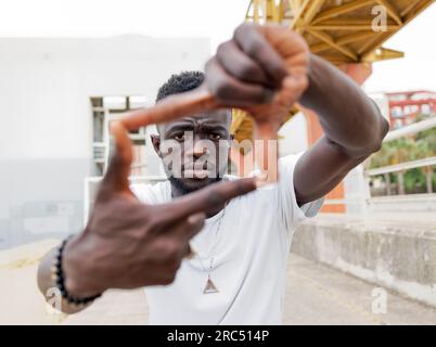 Giovani afro-americani con la barba, millennial, con abiti casual che fanno gesti di inquadratura e guardano la macchina fotografica sulla strada della città Foto Stock