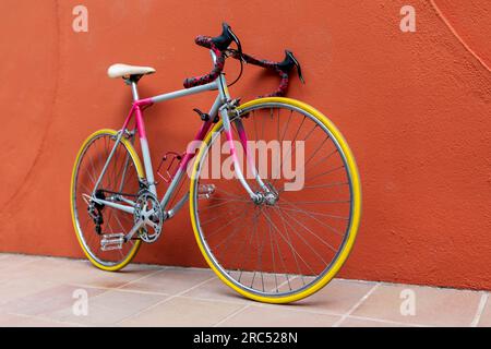 Dall'alto della moderna bicicletta da strada con telaio blu rosa sedile bianco gomme gialle appoggiate su un muro arancione in strada sul marciapiede in estate Foto Stock