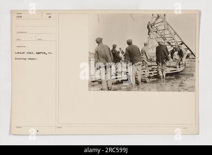 I soldati a Langley Field ad Hampton, Virginia, si trovano di fronte a un hangar, forse discutendo della loro missione o organizzando rifornimenti. L'hangar porta il simbolo dell'esercito americano, servendo come promemoria della loro dedizione e impegno durante la prima guerra mondiale. Foto Stock