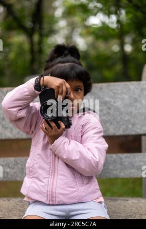 Una giovane ragazza possiede una fotocamera reflex digitale e guarda attraverso il mirino, scattando foto del mondo che la circonda. Foto Stock