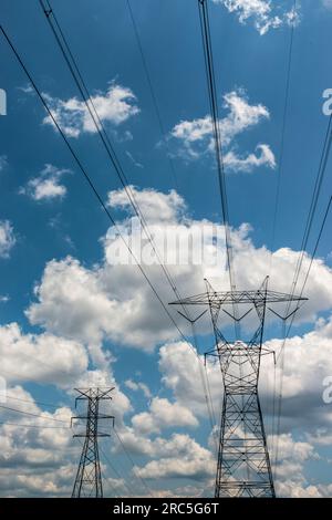 Immagine verticale di linee elettriche con nuvole di gonfiori bianche e cielo blu. Foto Stock