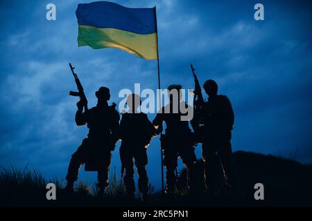 Una foto serale di guerrieri ucraini con i loro fucili che reggono una bandiera nazionale Foto Stock