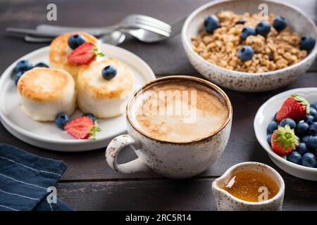 Cappuccino al caffè, frittelle al formaggio e muesli per colazione. Vista ravvicinata Foto Stock