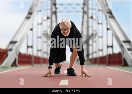 Uomo anziano in posizione di partenza in posizione di corsa all'aperto Foto Stock