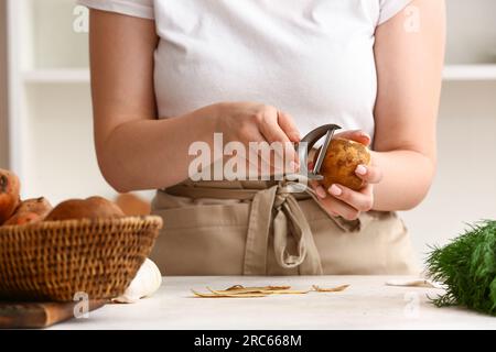 Donna di pelatura patate crudo a tavola in cucina Foto Stock